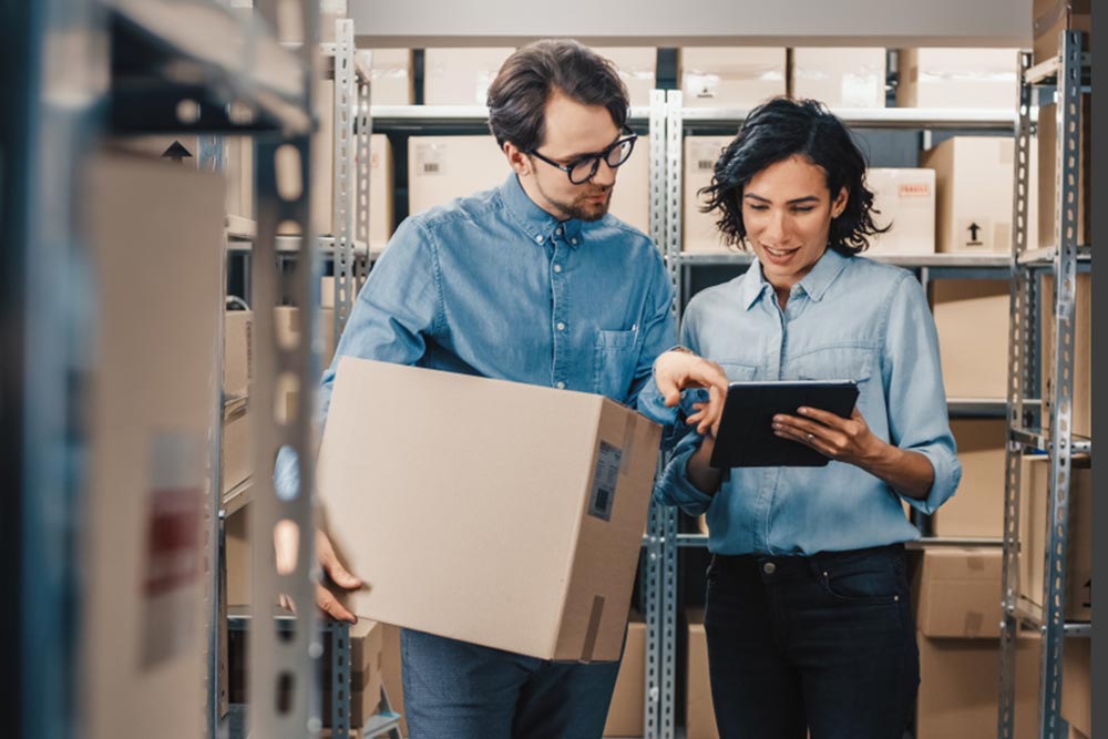 Female Inventory Manager Shows Digital Tablet Information to a Worker Holding Cardboard Box
