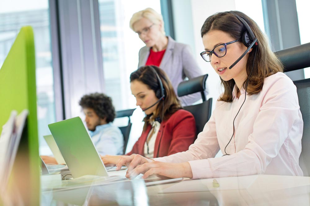 Female customer service representative using laptop while colleagues in background at office