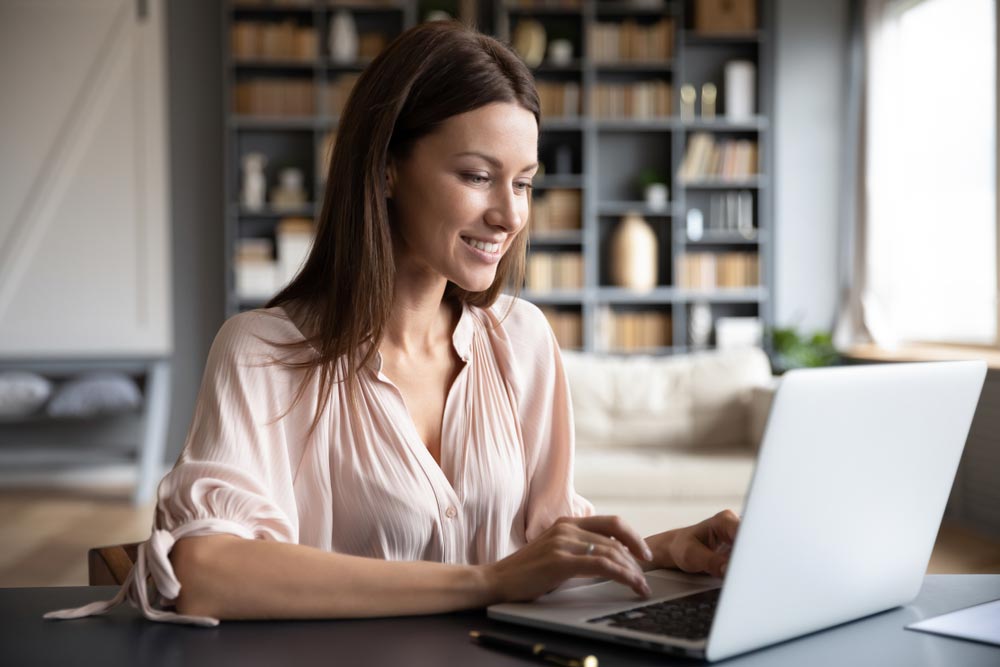 Happy young woman sit at desk look at laptop screen
