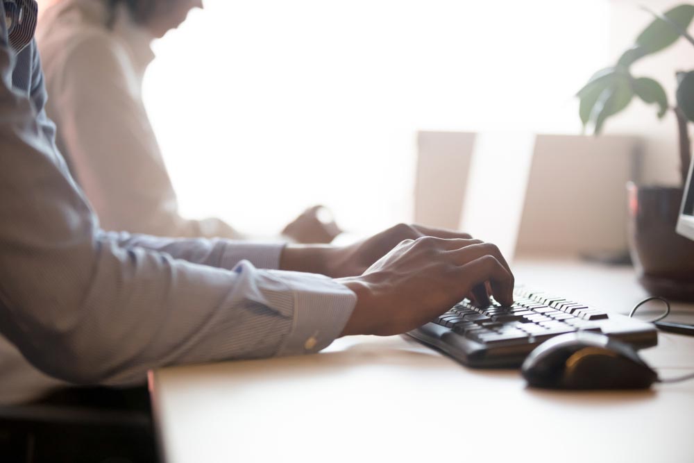 male company employee working on computer typing on keyboard sitting at office desk
